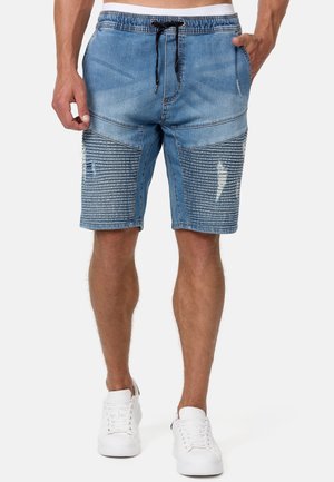 Shorts en jean de couleur bleu clair avec une taille à cordon de serrage, des détails effilochés et des accents côtelés verticaux à l'avant inférieur. Baskets blanches.