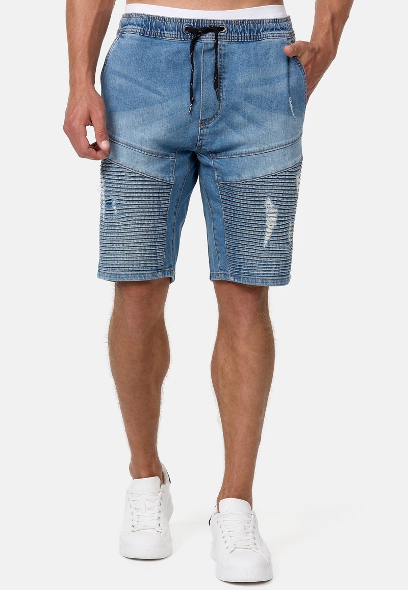 Shorts en jean de couleur bleu clair avec une taille à cordon de serrage, des détails effilochés et des accents côtelés verticaux à l'avant inférieur. Baskets blanches.