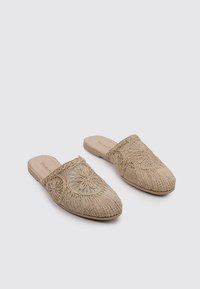 Mules tissés beiges avec broderie florale sur le dessus. Forme de pointe et semelle plate. Matériau texturé avec un design à dos ouvert.