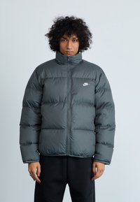 Tumehall puffer-jakk musta kõrge kraega, lukuga ja valge Nike logo rinna kohal. Horisontaalne tikandimuster ja sile tekstuur.