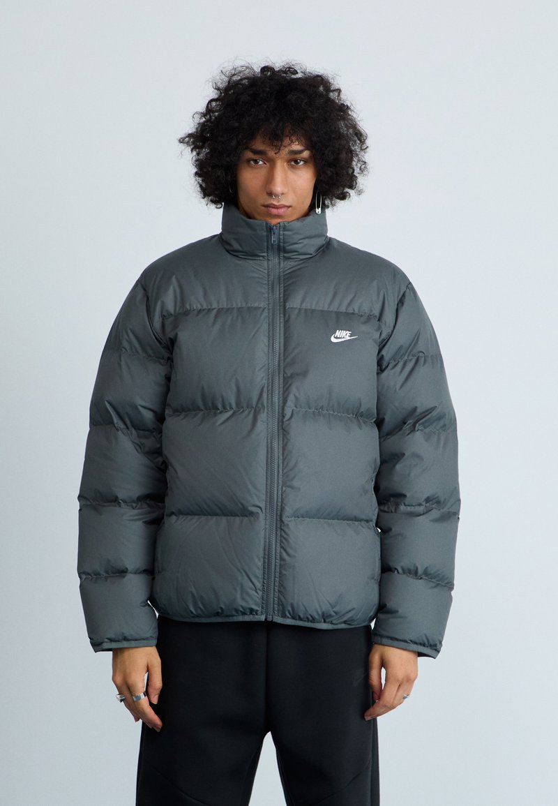 Tumehall puffer-jakk musta kõrge kraega, lukuga ja valge Nike logo rinna kohal. Horisontaalne tikandimuster ja sile tekstuur.