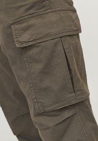 Pantaloni cargo din țesătură verde măslinie, având buzunare laterale mari, cusături vizibile și o textură moi. Concepuți cu o croială lejeră.