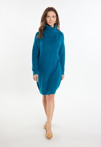 Rochie tricotată de culoare teal, cu guler înalt, mâneci lungi și o croială lejeră. Prezintă un finisaj texturat și o margine ușor curbată.