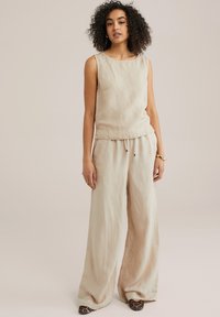 Haut sans manches en lin beige associé à un pantalon large beige. Tissu léger avec une texture lisse, doté d'une taille à cordon.