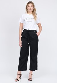 Hvid t-shirt med teksten "FEMME FATALE", parret med høj taljede sorte bukser med snøre og forlommer.