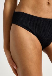 Högmidjad svart bikinibyxor i ribbad textur, med en bred midja och släta kanter för komfort och passform.