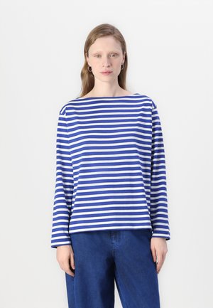 Chemise à rayures bleues et blanches à manches longues avec un col bateau, présentant une coupe ample. Associée à un pantalon bleu, avec des détails minimalistes.