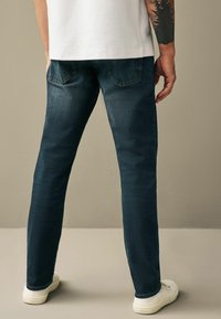 Jeans din denim închis, cu un croi drept, dotate cu buzunare la spate și o ușoară strălucire. Asortate cu adidași albi.