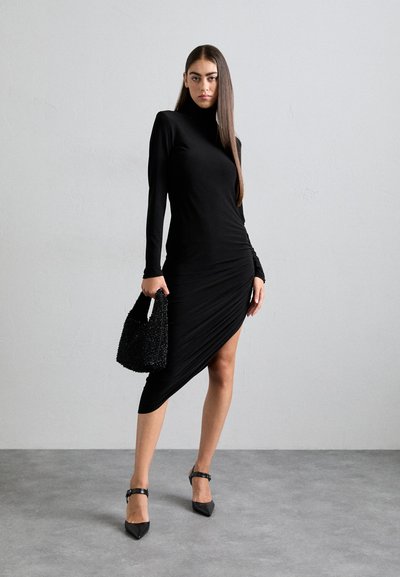 Rochie neagră cu mânecă lungă, cu o siluetă ajustată, hem asimetric și detalii pliate. Accesorizată cu o geantă texturată neagră și tocuri.