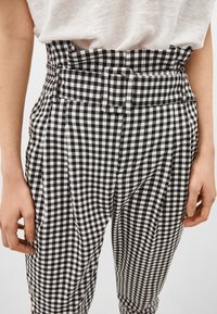 Schwarz-weiß karierte Hose mit hoher Taille, gefaltetem Vorderteil und Gürtelschlaufenakzenten, aus einem glatten Stoff gefertigt.