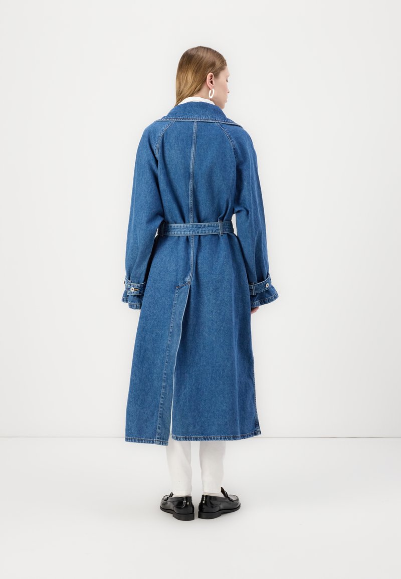 Langer Denim-Trenchcoat mit tailliertem Gürtel, vorderen Schlitzen und umgeschlagenen Ärmeln. Verfügt über einen klassischen Kragen und einen mittelblauen Farbton.