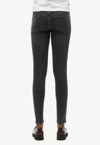 Jeans ajustados en denim gris oscuro, con costuras mínimas, dos bolsillos traseros y una textura suave. Combinados con zapatos negros.