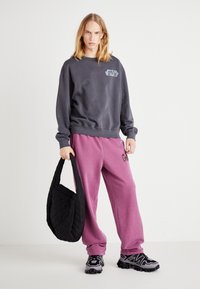 Felpa grigia scura con logo "Star Wars", abbinata a pantaloni della tuta rosa larghi e una borsa a tracolla nera trapuntata, con tessuto testurizzato e sneakers chunky.