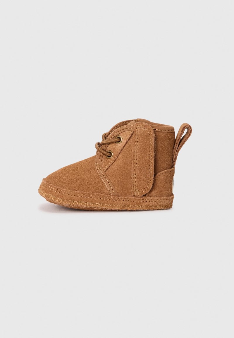 Chaussure bébé en daim marron avec lacets et bande velcro sur un fond uni gris clair.