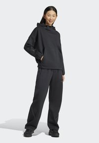 Crna dukserica s kapuljačom i odgovarajuće trenirke od mekog materijala. Ima prednji džep, opušten kroj i suptilne oznake brenda.