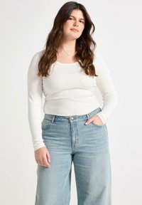 Maglietta a maniche lunghe bianca con righe abbinata a jeans a vita alta blu chiaro con taglio dritto classico e design a cinque tasche.