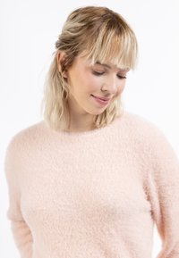 Lichtroze, fluffy trui met een ronde halslijn, zachte textuur en een ontspannen pasvorm. De mouwen lopen iets taps toe bij de manchetten.
