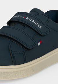 Тъмносиня маратонка с две велкро ленти, бяла подметка и лого на Tommy Hilfiger на каишката и отстрани.