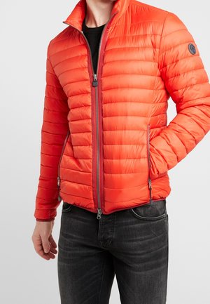 Veste en duvet rouge, design matelassé, fermeture éclair à l'avant, poches latérales et col haut. Le matériau semble lisse et léger.