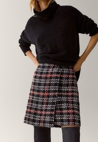 Zwarte trui van een wolmix met een col, gecombineerd met een zwart-wit geruite rok met rode accenten en een zijplooidetail.