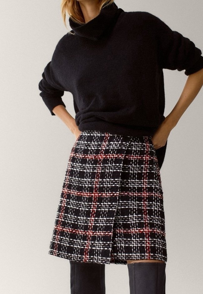 Zwarte trui van een wolmix met een col, gecombineerd met een zwart-wit geruite rok met rode accenten en een zijplooidetail.