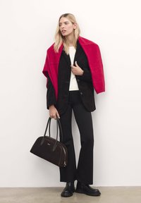 Blazer din suede negru peste un pulover alb, asortat cu pantaloni negri evazați. Ține o geantă maro, având o eșarfă roșie drapată. Botine negre.