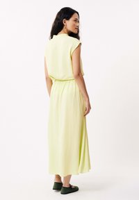 Robe maxi en lin jaune clair avec des manches courtes, taille cintrée et silhouette fluide. Assortie à des chaussures vertes à enfiler.
