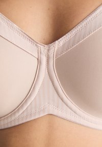 Beige bra with smooth fabric, incorporating a striped design. Features seam details and a V-shaped neckline, focusing on minimal hardware.