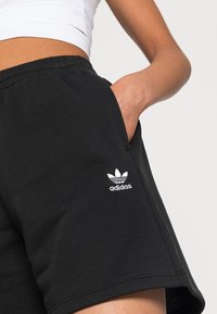 Svarta bomullsshorts med resårmidja, med sidofickor och en vit Adidas-logotyp på vänster lår.