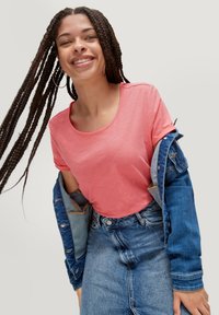 T-shirt rose à manches courtes avec un col rond, associé à une veste en jean bleu clair et une jupe en jean bleu. Cheveux longs tressés visibles.