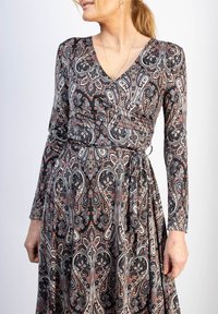 Pitkähihainen kietaisumekko mustana, jossa on paisley-kuvio punaisella, kermansävyisellä ja sinisellä. Mekossa on V-pääntie ja solmittava vyötärötieto. Pehmeä kangastuntuma.