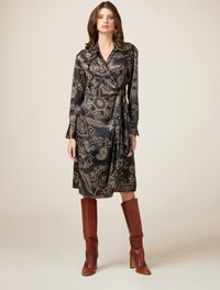 Rochie neagră tip wrap cu motive florale aurii, cu mâneci lungi și talie legată, asortată cu cizme din piele maro până la genunchi. Textură netedă.