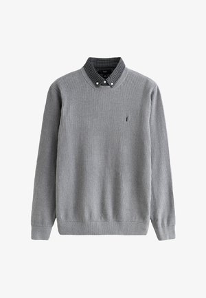 Pilkos spalvos megztinis su iškiliais briaunuotais raštais, apvalia iškirpte, ilgomis rankovėmis ir žvilgsnį traukiančiu juodo ir balto languoto marškinio apykakliu. Krūtinėje mažas logotipas.