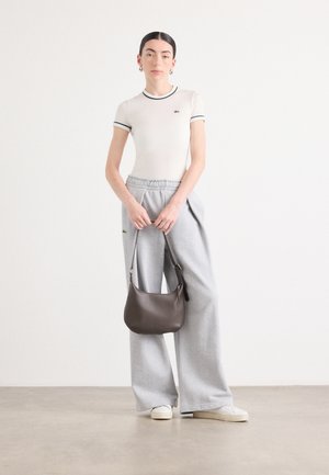 Light grey oversized sweatpants with an elastic waistband, paired with a fitted cream top featuring green trim and a small logo, complemented by a brown handbag.