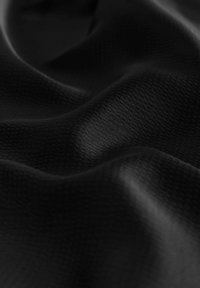 Fekete szövet sima textúrával és finom mintázattal, amelyen lágy redők és gyengéd hajlatok mutatkoznak.