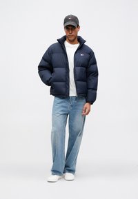 Ναυτική τζάκετ πούφ με ψηλό γιακά, κλείσιμο με φερμουάρ και λογότυπο. Συνδυασμένο με λευκό T-shirt, ανοιχτόχρωμα μπλε τζιν και λευκά παπούτσια.