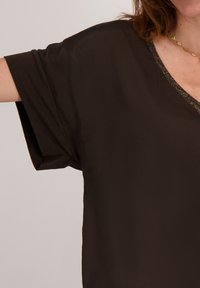 Zwarte, losse top met een V-hals en korte mouwen. Heeft een subtiele, getextureerde rand langs de hals. Zachte stof.