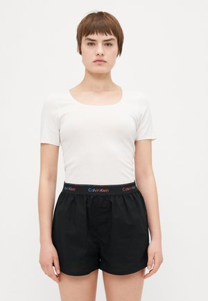 Haut blanc à manches courtes avec un col rond associé à un short en coton noir doté d'une ceinture élastique Calvin Klein colorée.