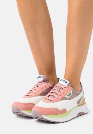 Scarpe atletiche rosa e bianche realizzate in materiali scamosciati e in rete, con una suola bianca spessa e dettagli verde chiaro. Logo sulla linguetta.