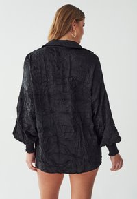 Zwarte oversized, gekreukelde blouse met kraag, lange mouwen en goed passende manchetten. Toon een gestructureerde stof en een ontspannen silhouet.