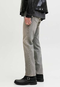 Jeans de mezclilla gris con ajuste relajado, que presentan un diseño clásico de cinco bolsillos y costuras en contraste, combinados con botines negros de cuero.