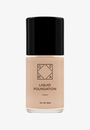 Flytande foundation i en klar glasflaska med svart lock. Etiketten har varumärkets initialer och produktnamnet i fet svart text. 30 ml.