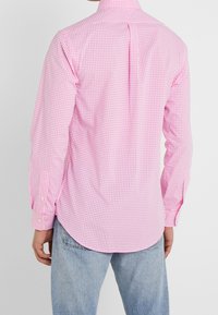 Růžová kostkovaná košile s dlouhým rukávem a límcem na knoflíky, s yoke a zaobleným lemem; v kombinaci se světlými modrými džíny.