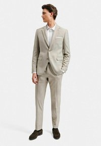 Beige kostym med slim fit, som har en tvåknappsblazer, raka byxor och en vit skjorta. Accentuerad med en bröstficka och bruna skor.