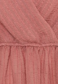 Rosa klänningsstoff med vertikala ränder och en texturerad yta. Tyget är samlat vid midjan, vilket skapar en flödande silhuett.