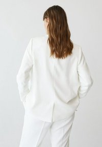 Witte op maat gemaakte blazer met een gladde textuur, gestructureerde schouders, lange mouwen en een middenventilatie, gecombineerd met een bijpassende witte broek.