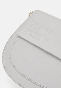 Graue Leder-Clutch mit strukturiertem Oberflächen, geschwungener Klappenform, eingeprägtem Logo und einem Metallring-Detail.