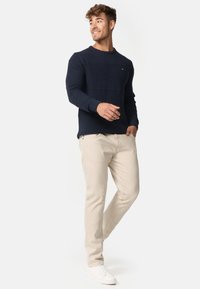 Navy gebreide trui met textuurontwerp, crème chino's en witte sneakers. Zichtbaar logo op de trui; relaxte pasvorm.