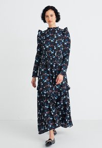 Vestido preto de mangas longas com um design de babados, apresentando um padrão floral em azul e bordô, com um decote alto e saia em camadas.