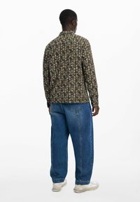 Tumedast rohelisest kangast pikkade varrukatega särk, millel on mitmevärviline geomeetriline muster, koos lahtiste siniste teksade ja heledate tossudega.